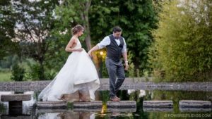The bride and groom carefully cross a pond