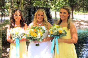 Three bridesmaids in yellow dresses standing next to a pond.