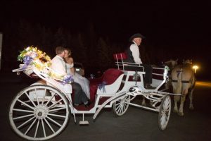 A bride and groom riding in a horse drawn carriage at night.