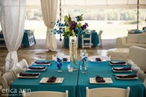 A table set up in a tent with blue and purple tablecloths.