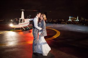 A bride and groom kiss in front of a helicopter at night.