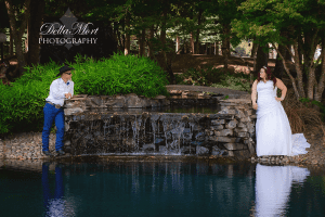 A bride and groom standing next to a pond in the woods.