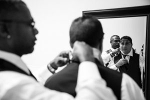 A man is adjusting his tie in front of a mirror.