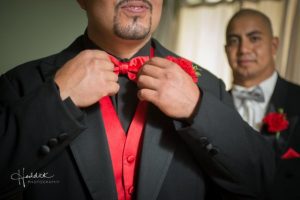 A man in a tuxedo is adjusting his bow tie.