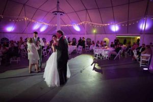 A bride and groom dance in a tent with purple lights.