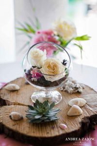 A glass bowl filled with flowers and shells on top of a cabana by the beach.