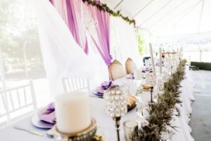A table set up in a tent with purple and white decorations.