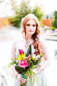 A bride in a green dress holding a bouquet of tropical flowers.
