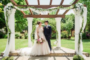 A bride and groom standing under a pergola in a garden.