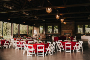 A wedding reception set up with white tables and red chairs.