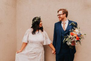 Newlyweds hold hands in front of a wall