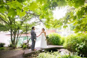 A bride and groom standing on a bridge, finding design inspiration in the shady garden grove surrounding them.