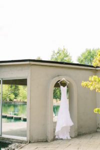 A beach wedding dress hanging outside of a building near a pond.