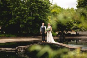 A bride and groom enjoying a romantic moment on a bridge near a tranquil pond.