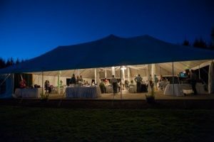 A large white tent with people sitting around it at night.