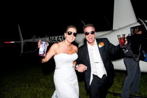 A bride and groom standing next to a helicopter.