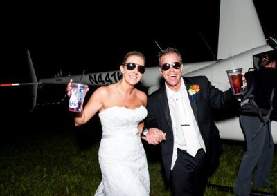 A bride and groom standing next to a helicopter.