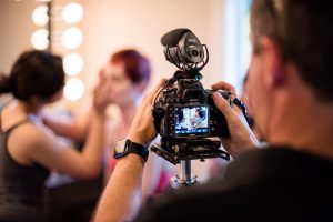 A man is taking a picture of a woman in front of a camera.