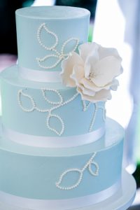 A blue and white wedding cake with a white flower.