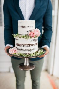 A man holding a wedding cake with flowers on it.