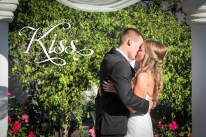 A bride and groom kiss in front of a gazebo.