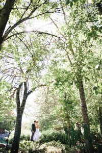 A bride and groom standing under a tree in a wooded area.