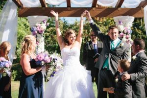 A bride and groom raising their hands in the air during their wedding ceremony.