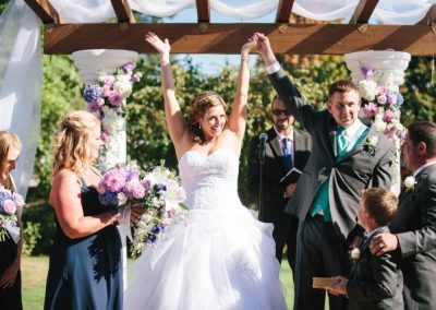 A bride and groom raising their hands in the air during their wedding ceremony.