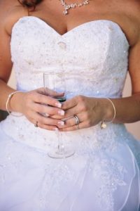 A bride in a wedding dress gracefully holds a glass of wine at an enchanting outdoor Oregon wedding venue.