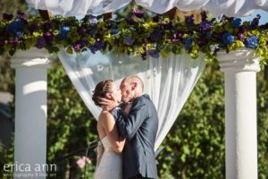 A bride and groom kiss under a pergola.