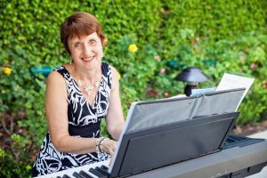 A woman sitting at a piano in front of bushes.