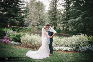 A bride and groom kissing in front of a pond.
