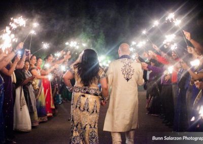 A bride and groom holding sparklers as they walk down the aisle.