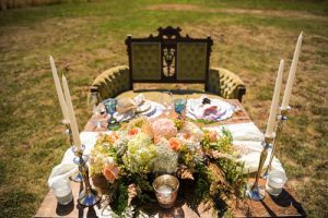 A table set up in a field with candles and flowers.
