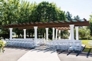 An outdoor wedding ceremony with white chairs and a pergola.