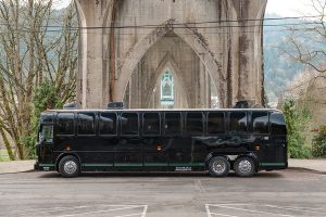 A black bus parked in front of a bridge.