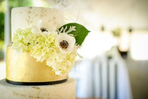 A gold and white wedding cake with flowers on top.
