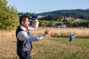 A groom throwing a hat in a field.