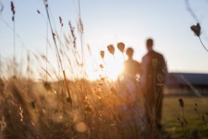 A bride and groom standing in tall grass at their enchanting Oregon outdoor wedding venue, basking in the golden hues of sunset.