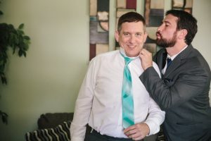 A man is putting his tie on a man in a suit.