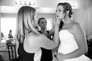 A bride is getting her makeup done by a bridesmaid.