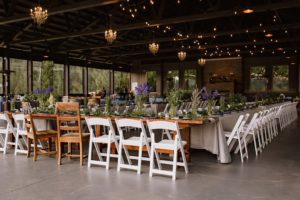 A long table set up with white chairs and flowers.