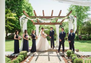 A group of bridesmaids and groomsmen standing under a pergola.