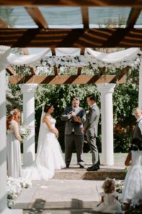 A bride and groom exchange vows under a wedding arbor.