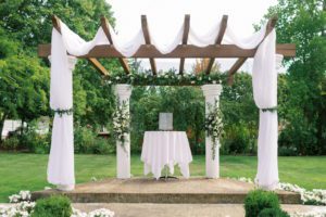 A wedding ceremony adorned with elegant white drapes and blossoming flowers featuring exquisite wedding arbor designs.