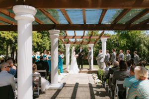 A wedding ceremony under a gazebo, adorned with beautiful Wedding arbor designs, in a garden.