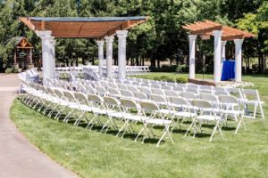 An outdoor ceremony set up with white chairs and a wedding arbor.