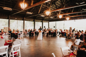 A bride and groom dance in a large barn.