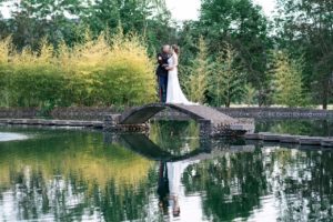 A bride and groom standing on a bridge over a pond, embracing their beach wedding design inspiration.