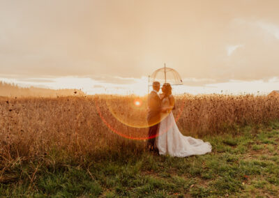 A bride and groom holding an umbrella at sunset